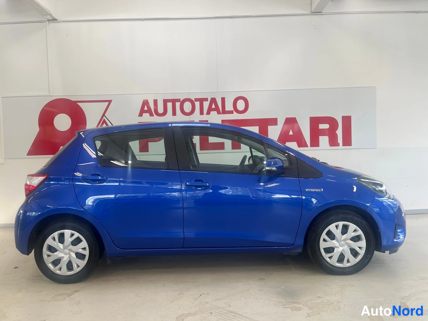 Sivulta: Sinisen Toyota Yaris -henkilöauton sivukuva oikealta, kuvattu sisätiloissa.