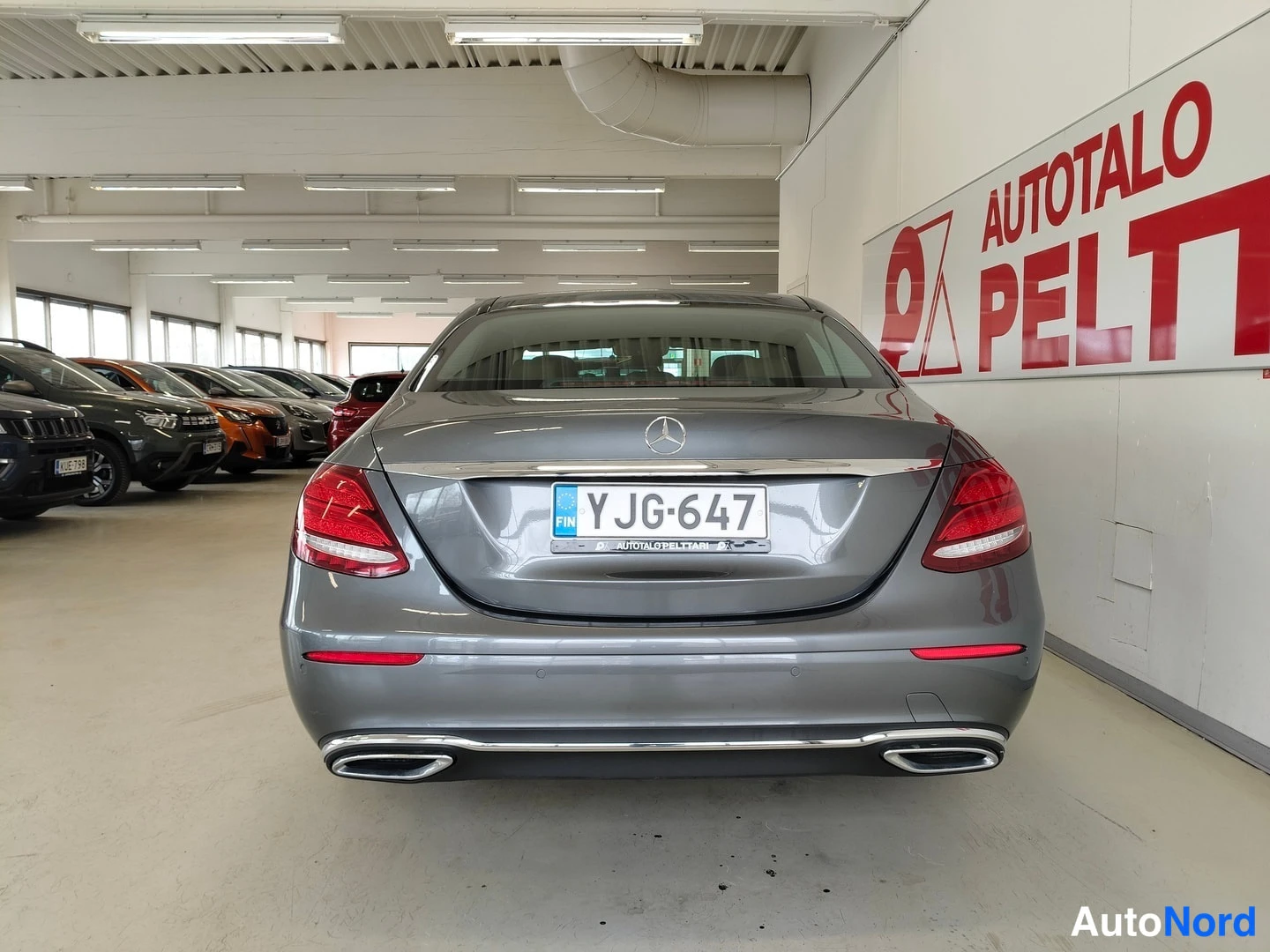 Takaa: Mercedes-Benz E-sarjan sedanin takaosa keskeltä takaa; rekisteri, harmaa kori ja kromilista kannen reunassa.