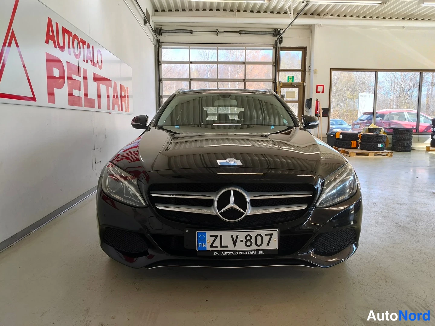 Edestä: Mustan Mercedes-Benzin keula suoraan edestä, Mercedes-tähti etusäleikössä ja rekisterikilpi.