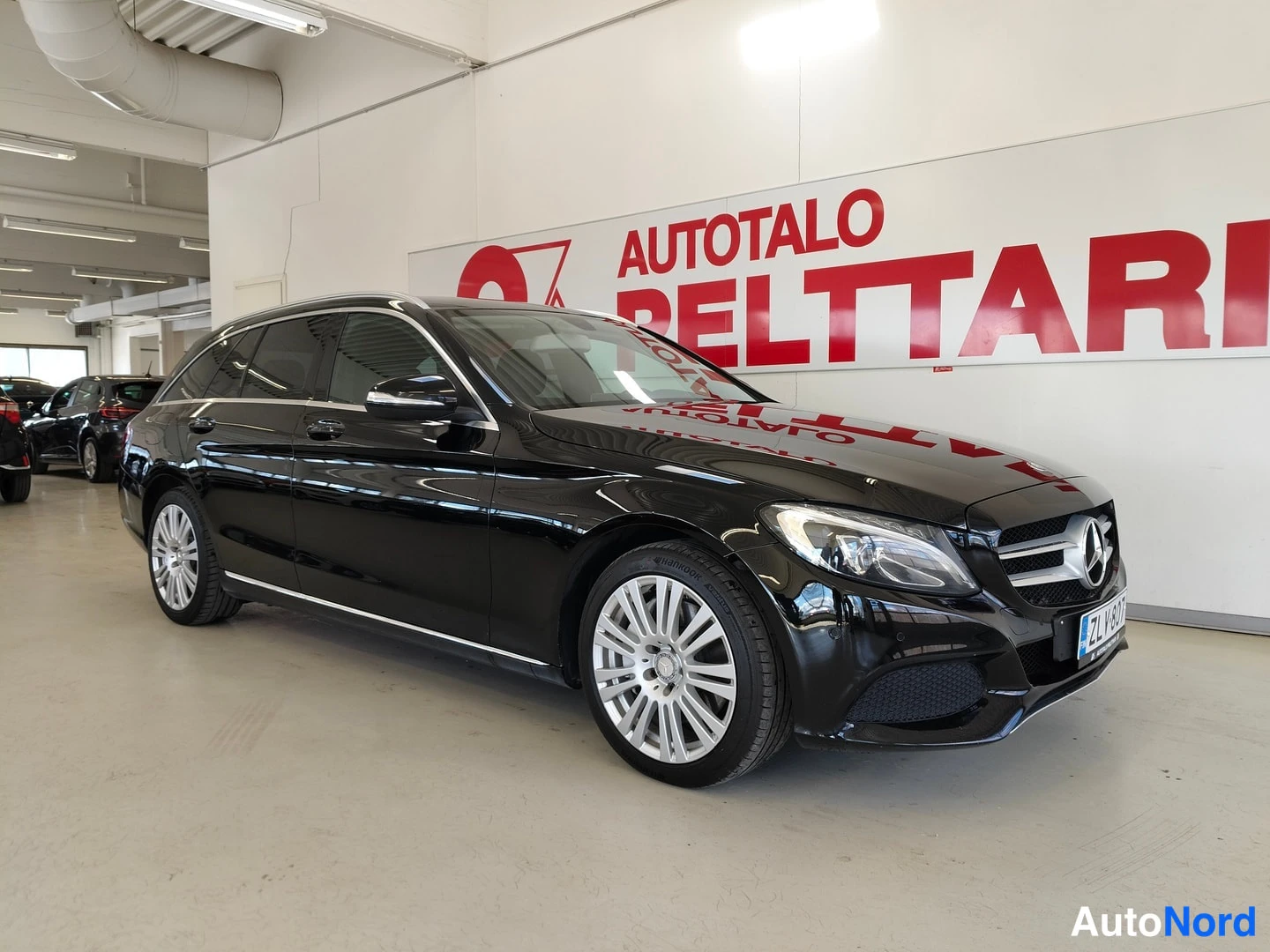 Etuviisto, nokka oikealle: Musta Mercedes-Benz C farmari edestä vinosti hallissa, etusäleikössä Mercedes-tähti.