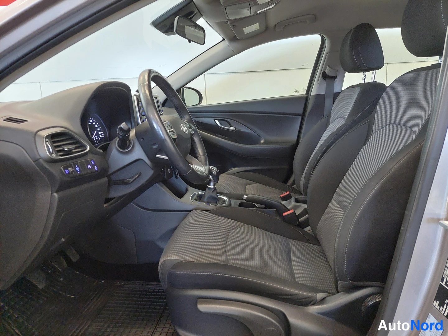 Muu: Hyundai i30 Farmrin ohjaamo nähtynä matkustajan puolelta: ratin ja kojelaudan lisäksi näkyvät molempien etupenkien kankaiset istuimet, manuaalivaihteen valitsin
