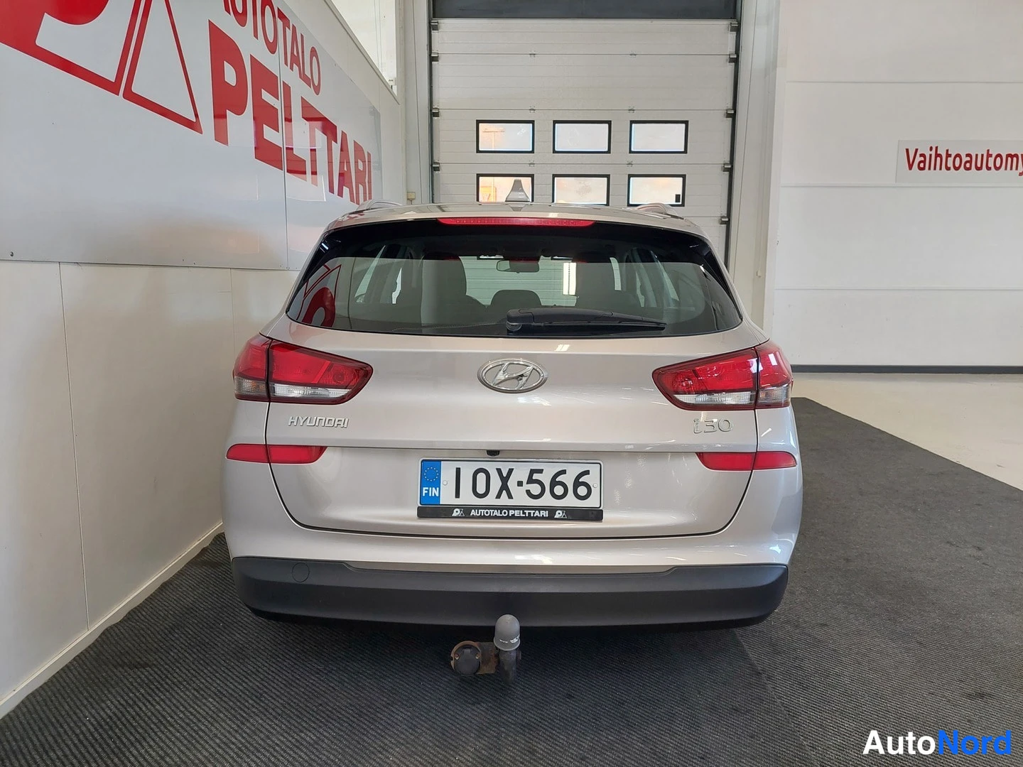 Takaa: Hyundai i30 rear view straight on in a garage, silver body, Hyundai and i30 badges, license plate 10X-566 and tow hitch visible.