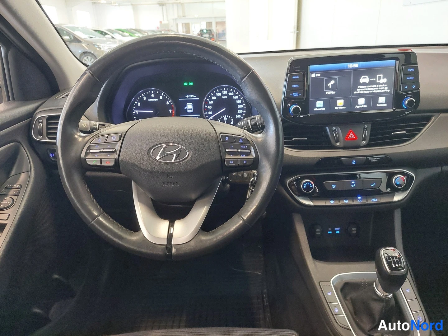 Muu: Close-up of Hyundai i30 driver's area: leather steering wheel with Hyundai logo, analogue gauges, touchscreen showing 10:56, climate controls and manual gear le