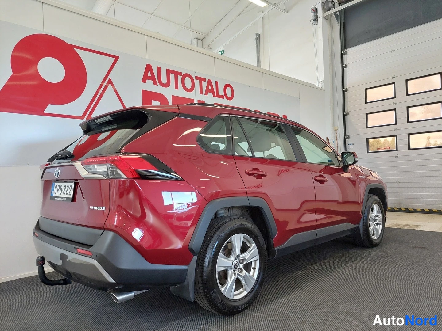 Takaviisto: Punaisen Toyota RAV4:n takakolmannes sisätiloissa, rekisterikilpi ja HYBRID-merkintä näkyvissä, vetokoukku takapuskassa.