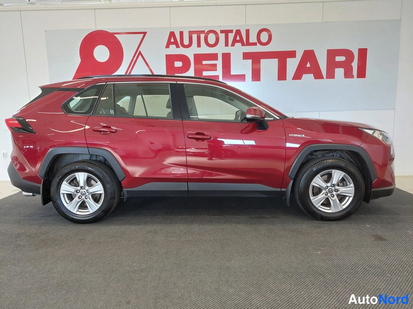 Sivulta: Punaisen Toyota RAV4:n sivuprofiili sisätiloissa, HYBRID-merkintä etulokasuojassa.
