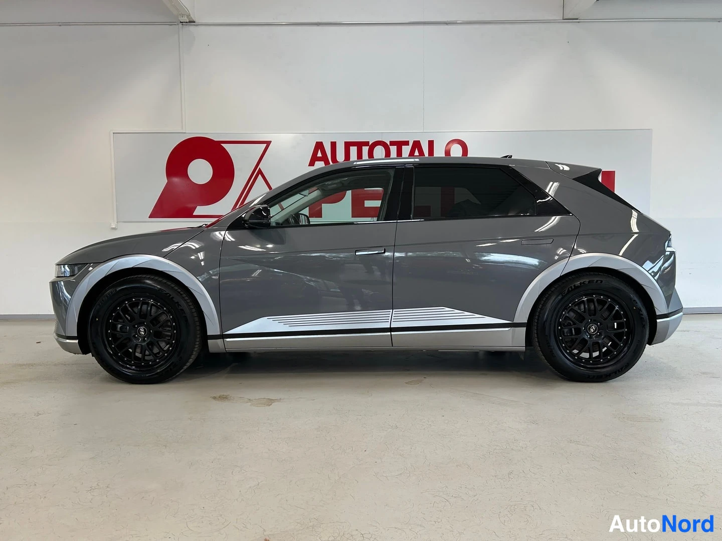 Sivulta: Harmaa Hyundai IONIQ 5 täysin sivusta, mustat kevytmetallivanteet ja hopeiset korosuojat.