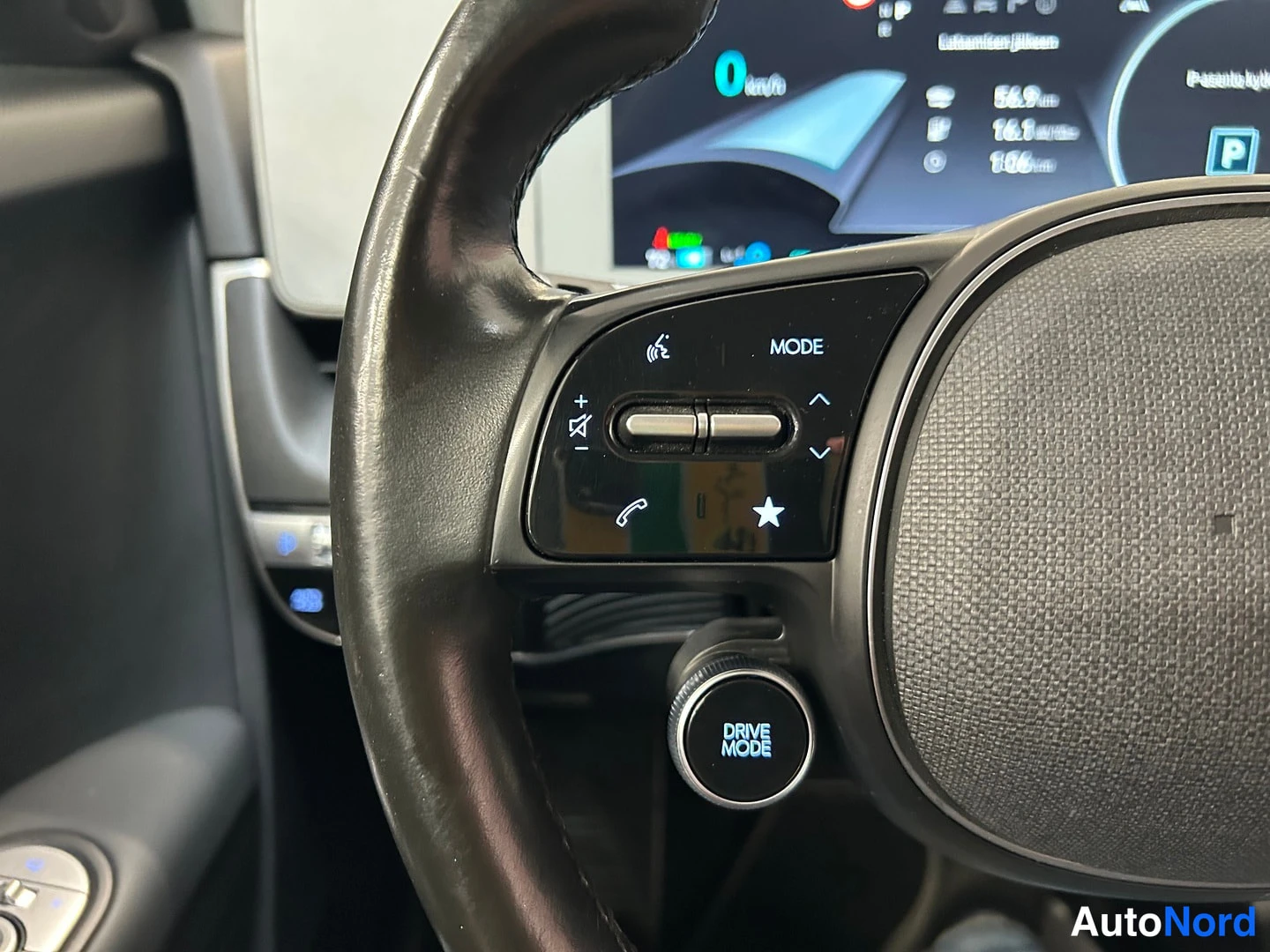 Muu: Hyundai IONIQ 5:n ratin vasemman pöykärin painikkeet ja DRIVE MODE -valitsin lähikuvassa, taustalla osa mittarinäytöstä.
