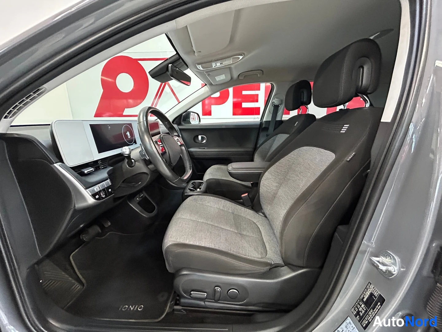 Muu: Hyundai IONIQ 5:n etusisätila ohjausistuimineen, mittaristön infotainment-näytöineen ja IONIQ-lattiamattoineen