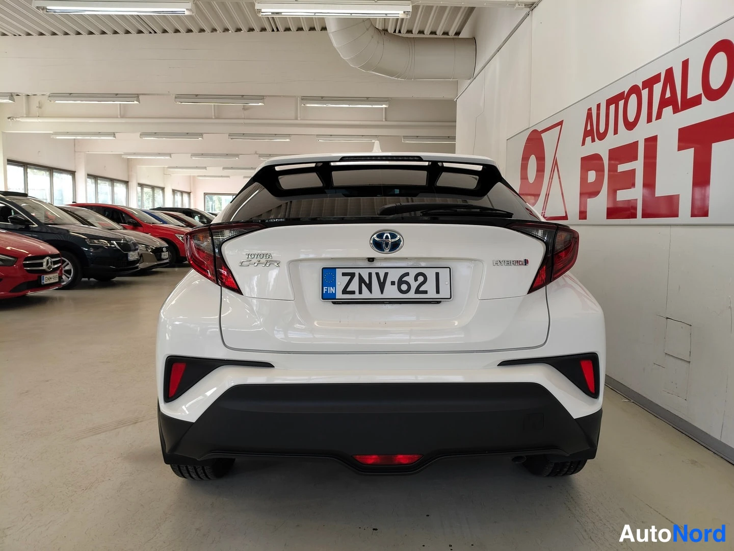 Takaa: Auton takanäkymä: valkoinen Toyota, rekisterikilpi, Toyota C-HR -merkinnät ja HYBRID-tunnus takaluukussa.