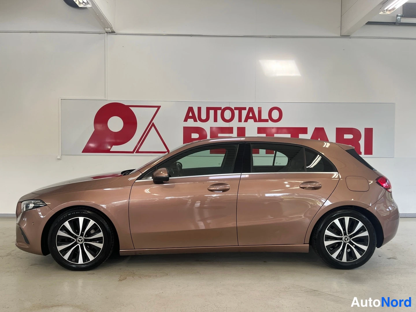 Sivulta: Mercedes-Benz A -henkilöauto suoraan sivulta vasemmalta kuvattuna; kulmikas siluetti, viisiovinen hatchback, alumiinivanteet, taustalla Autotalo Pelttari -maino