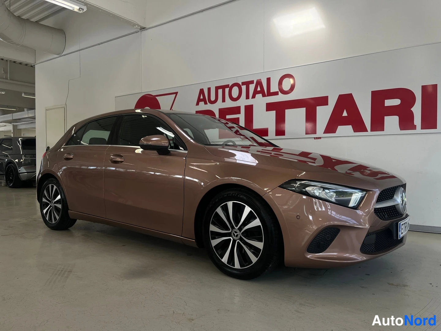 Etuviisto, nokka oikealle: Mercedes-Benz A-sarjan viistosti edestä oikealta kuvattu hatchback-autotallissa; korin väri kupariruskea.