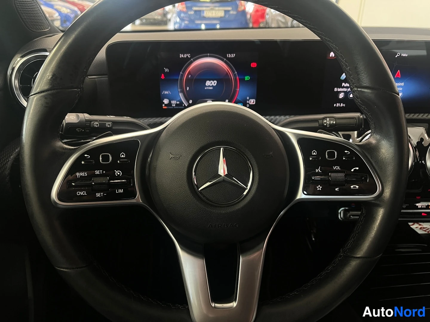 Muu: Lähikuva Mercedes-Benzin monitoimiohjauspyörästä ja digitaalisesta kojelaudasta, kilpi- ja infotainment-näkymät näkyvissä.