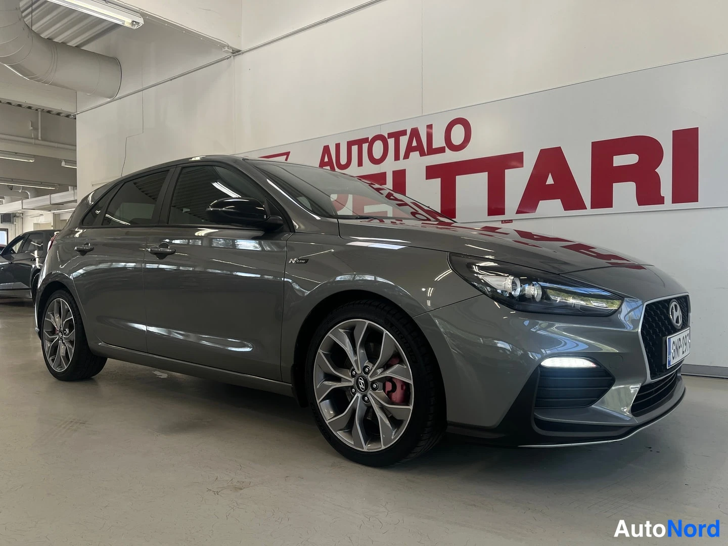 Etuviisto, nokka oikealle: Hyundai i30 -viistoperä edestä oikealta katsottuna, harmaa koripinta ja etusäleikkö näkyvissä.