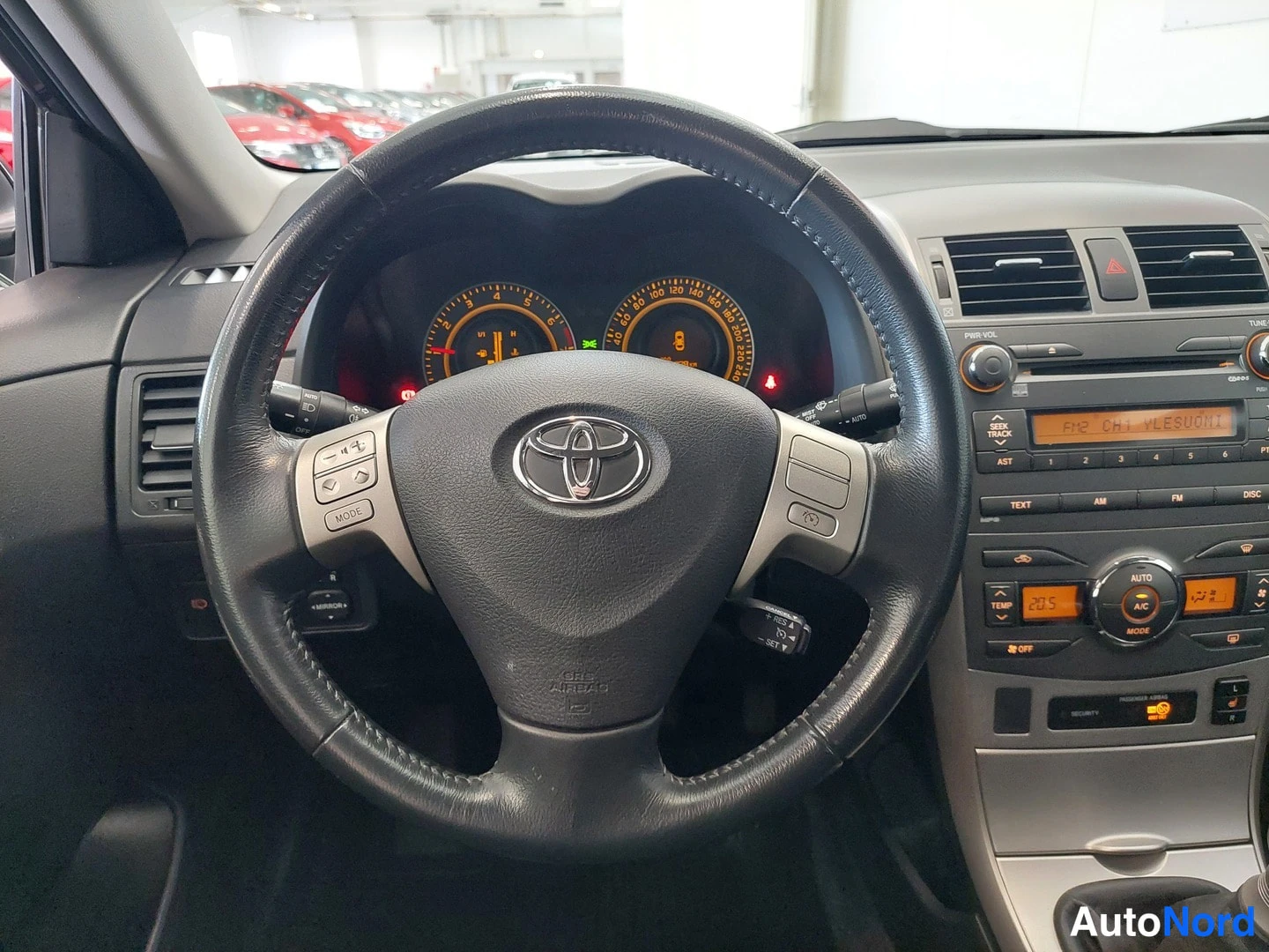 Yksityiskohta: Ohjaamo Toyota Corolla: musta riimu ohjauspyörä, analogiset mittarit ja keskuspaneelin radiopaneeli ja automaattinen ilmastointi (AC, AUTO, 22,5)