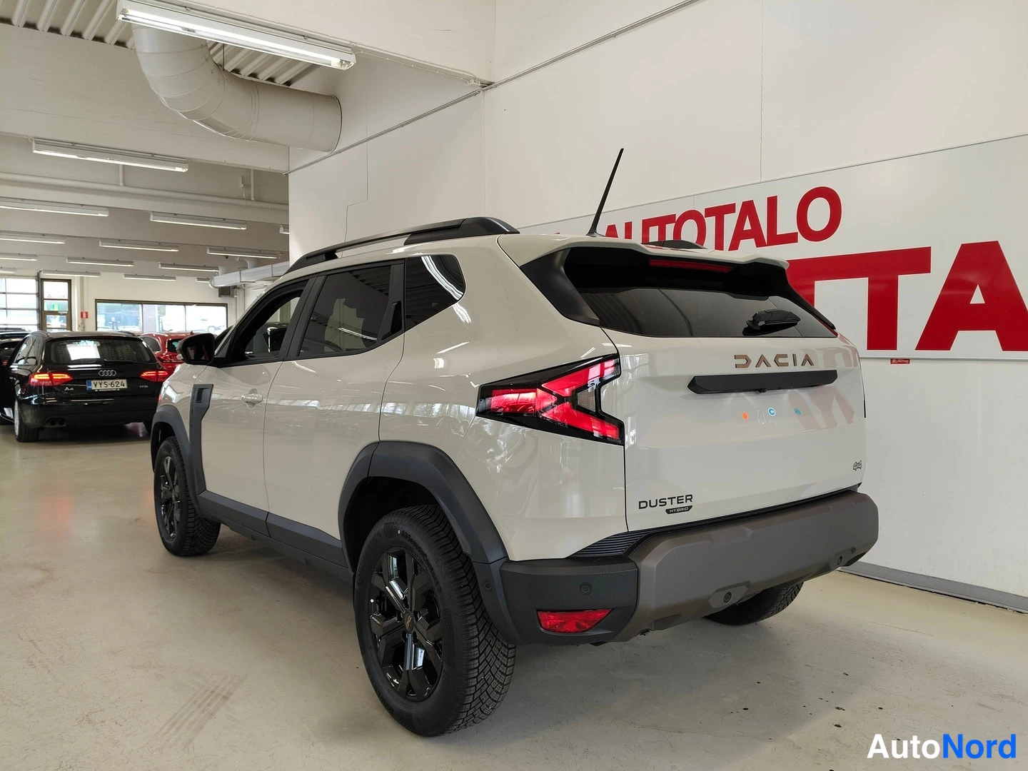 Takaviisto: Auto takakolmanneskulmasta kuvattuna; takapää ja vasen kylki näkyvissä, takaluukissa DACIA- ja DUSTER-tekstit, mustat vanteet.