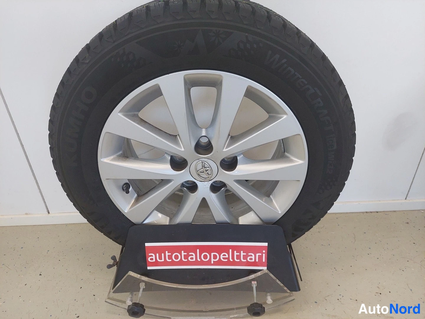 Yksityiskohta: Auton talvipyörä seisoo telineessä: hopeavanteessa on Toyotan merkki ja Nokian talvirenkaan sivussa lukee Nokian Tyres, Winter Snow-proof.