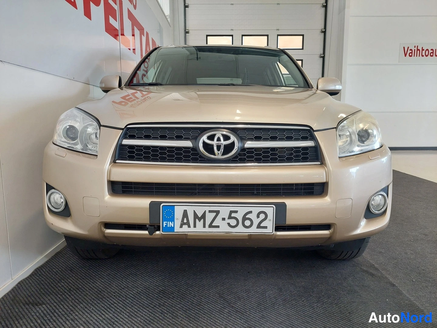 Edestä: Auto suoraan edestä kuvattuna sisätiloissa; Toyota-merkki etusäleikössä, sumuvalot puskurissa, rekisterikilpi.