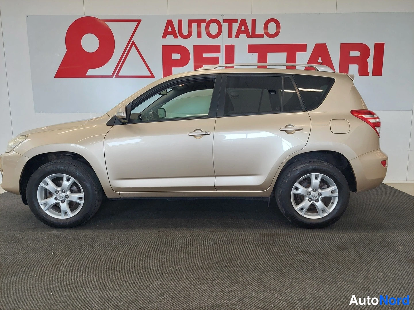 Sivulta: Kultautanvärinen Toyota RAV4 sivusuunnasta sisätiloissa, kylki ja pyörät näkyvissä.