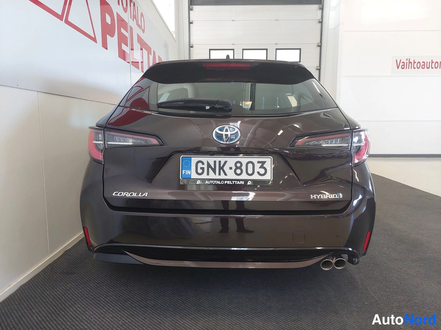 Takaa: Auton takaosa suoraan takaa kuvattuna, rekisterikilpi, toyotan logot ja HYBRIDI-teksti näkyvissä.