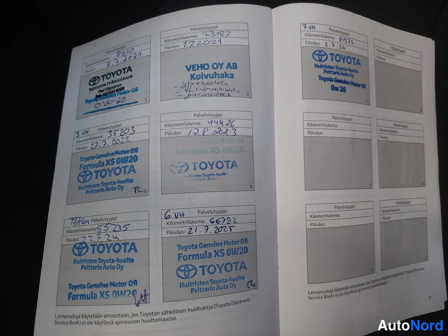Asiakirja: Avattu Toyota-huoltokirja, jossa käsinkirjoitetut huoltomerinnät kilometrilukuineen ja päivämäärineen.