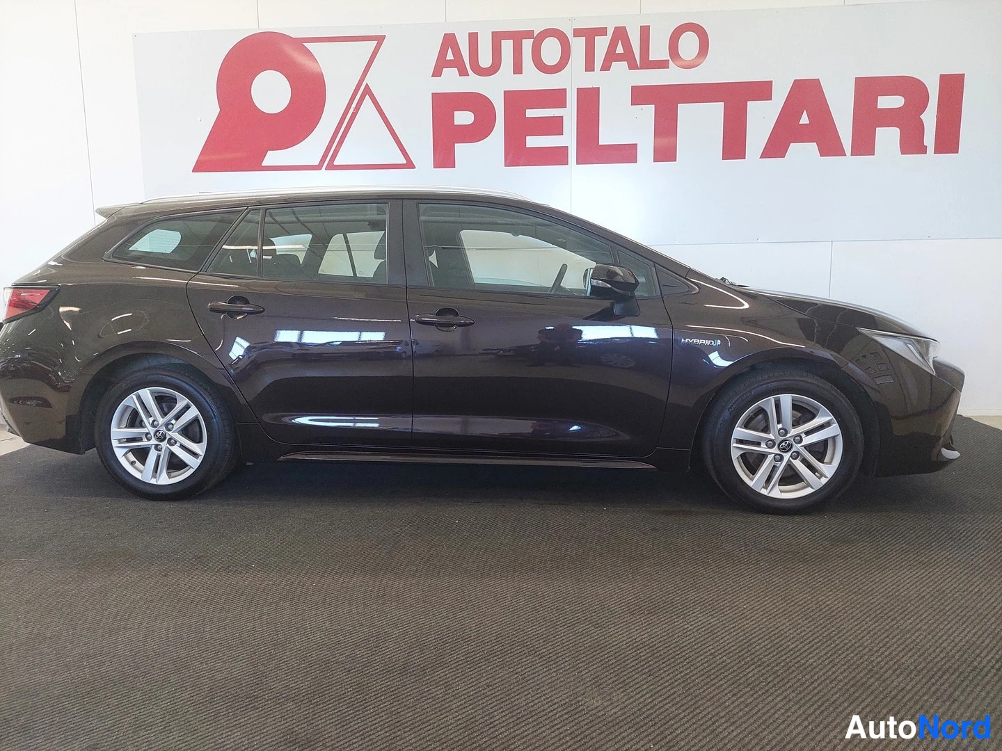 Sivulta: Auton sivuprofiili sisätiloissa; tummanruskea farmarikorinen Toyota, hopeaiset peltivanteet.