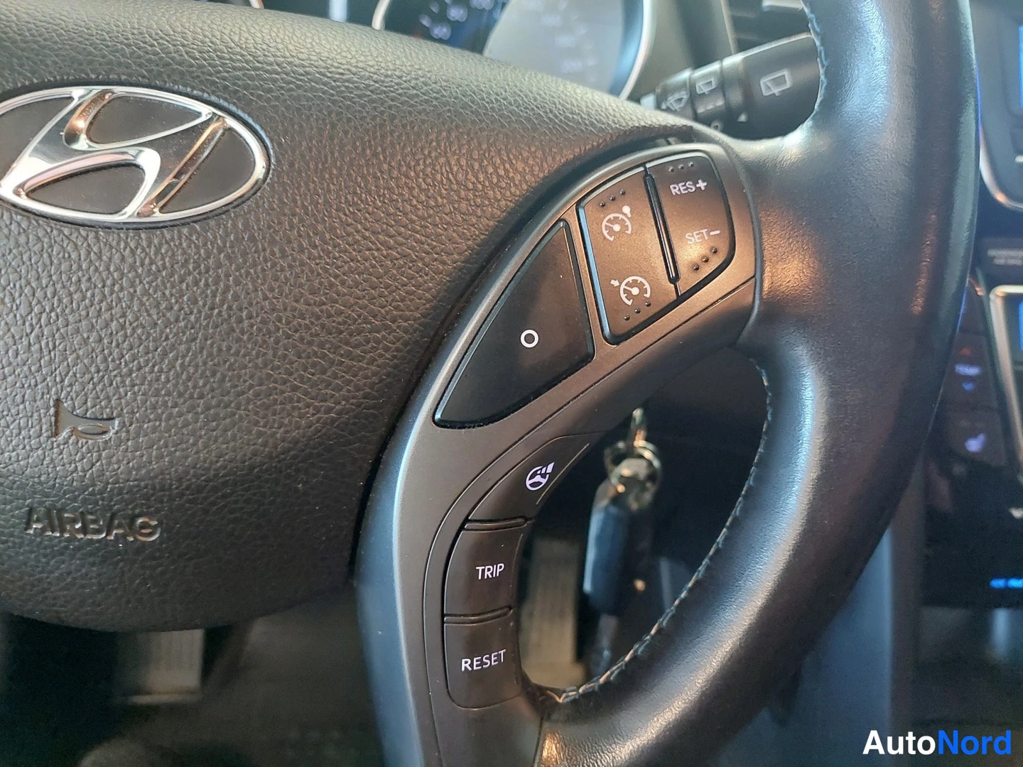 Muu: Hyundai-ohjauspyörän oikea puoli: rattipainikkeet RES+ ja SET- (vakionopeudensäädin) sekä TRIP- ja RESET-napit; sytytinavain on rattiin kytkettynä.