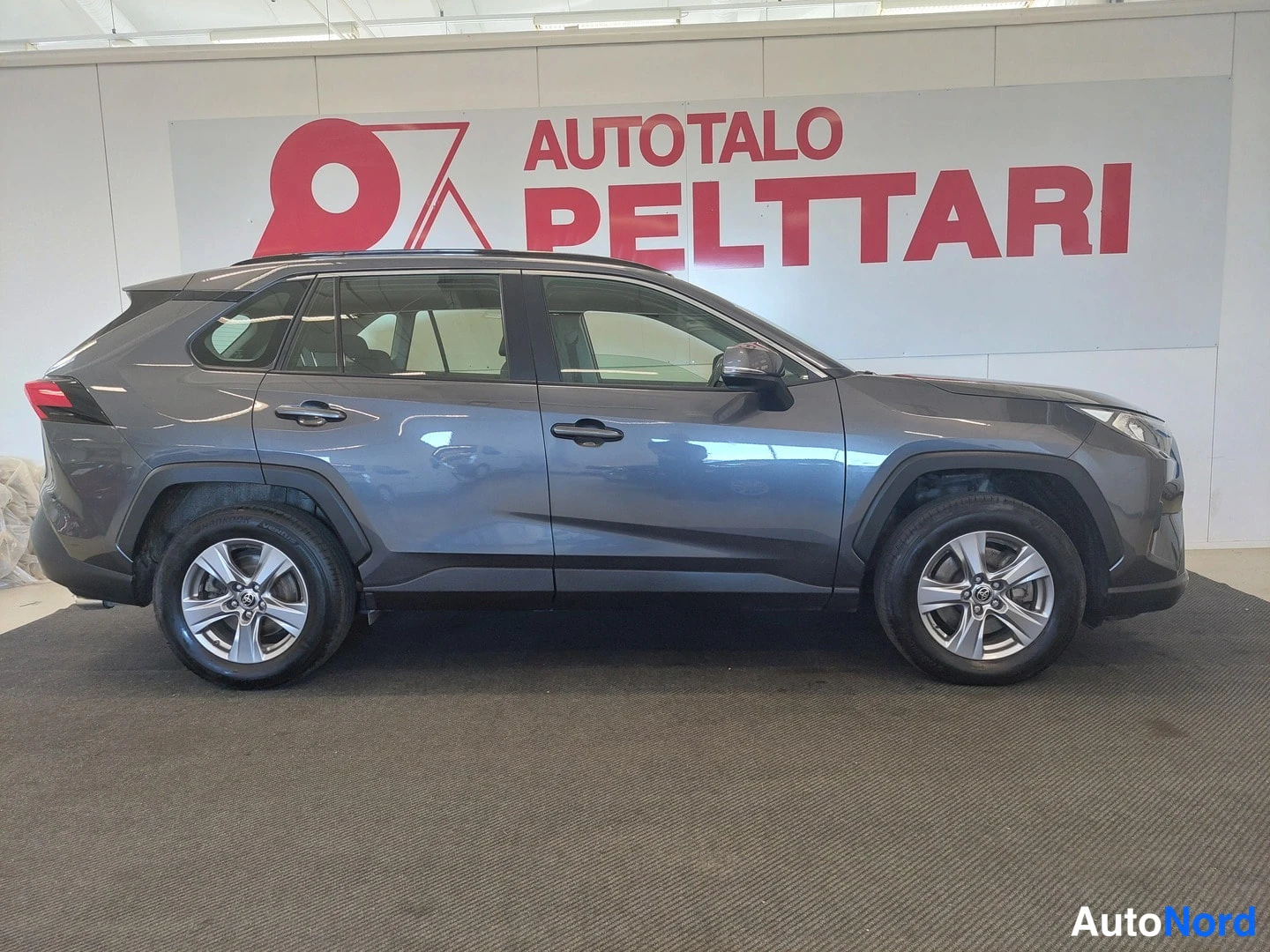 Sivulta: Toyota RAV4:n sivukuva oikealta puolelta sisätiloissa, tummanharmaa koripinta ja hopeavanteet näkyvät.