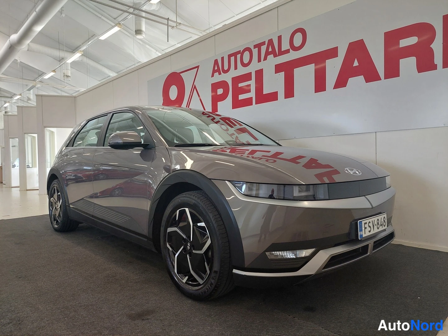 Etuviisto, nokka oikealle: Hyundai IONIQ 5:n keulaviisto oikealta; keulan grille, valot ja rekisterikilpi näkyvät, auto tummanharmaa.