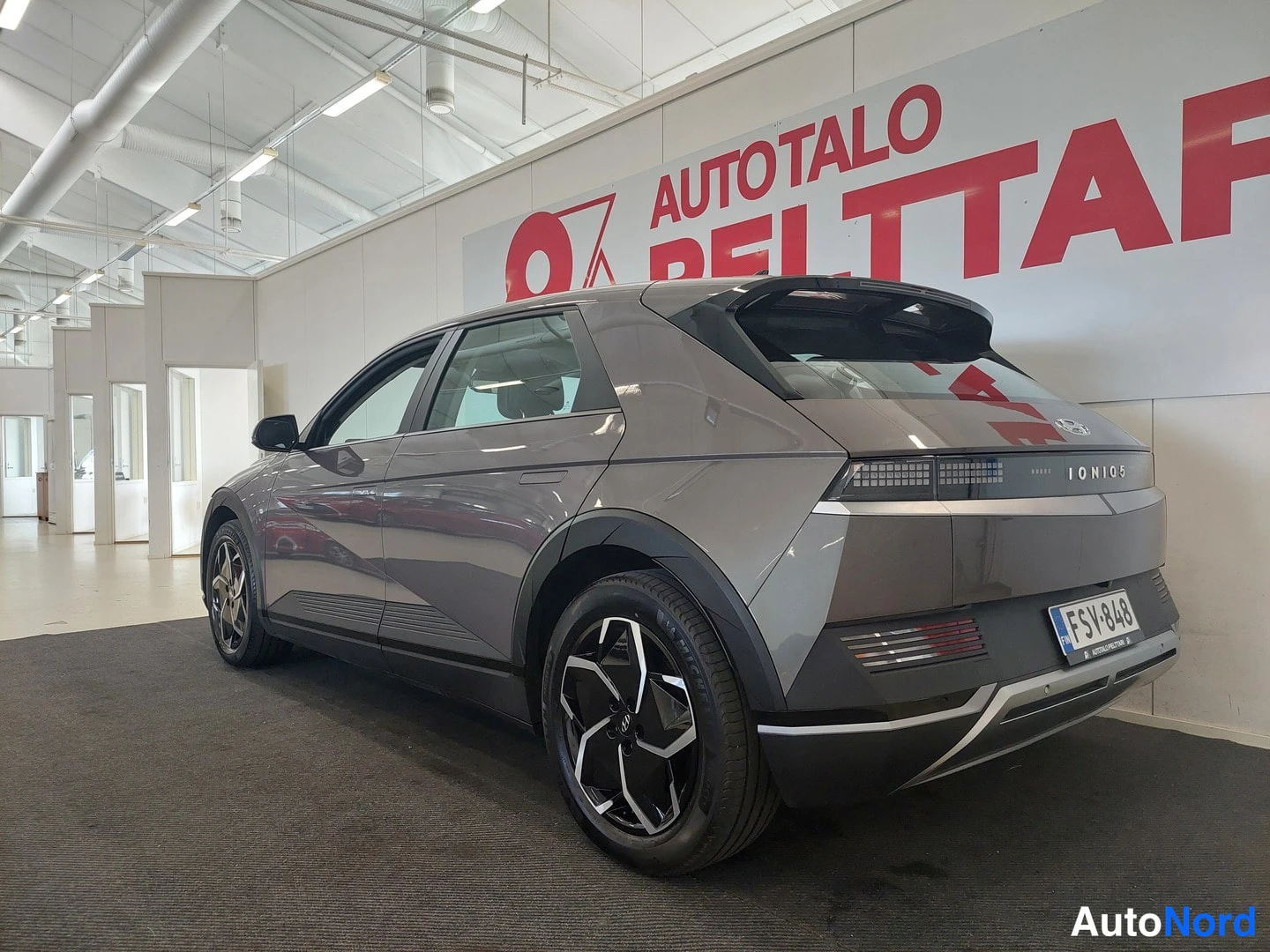 Takaviisto: Hyundai Ioniq 5 -farmariauto takaviistosta sisätiloissa, harmaakköinen kori ja tunnistekilpi.