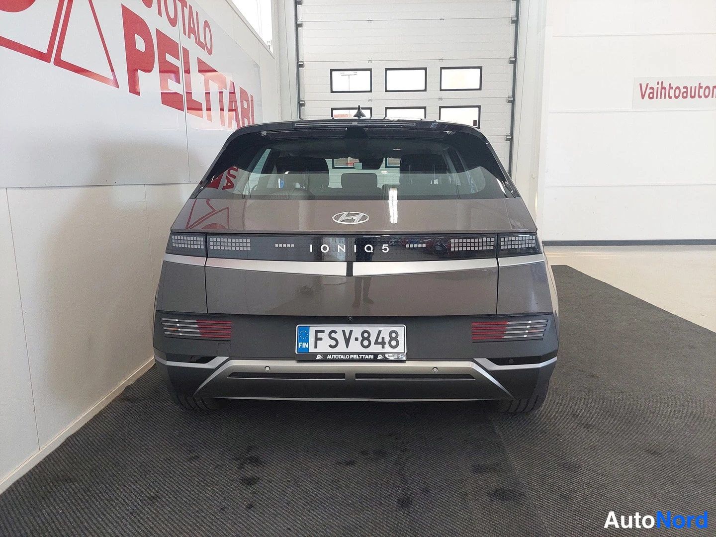 Takaa: Hyundai IONIQ 5:n takaosan suora vastakkainnäkymä sisätiloissa; rekisteritunnus ja IONIQ 5 -teksti näkyvät takanapeissa.