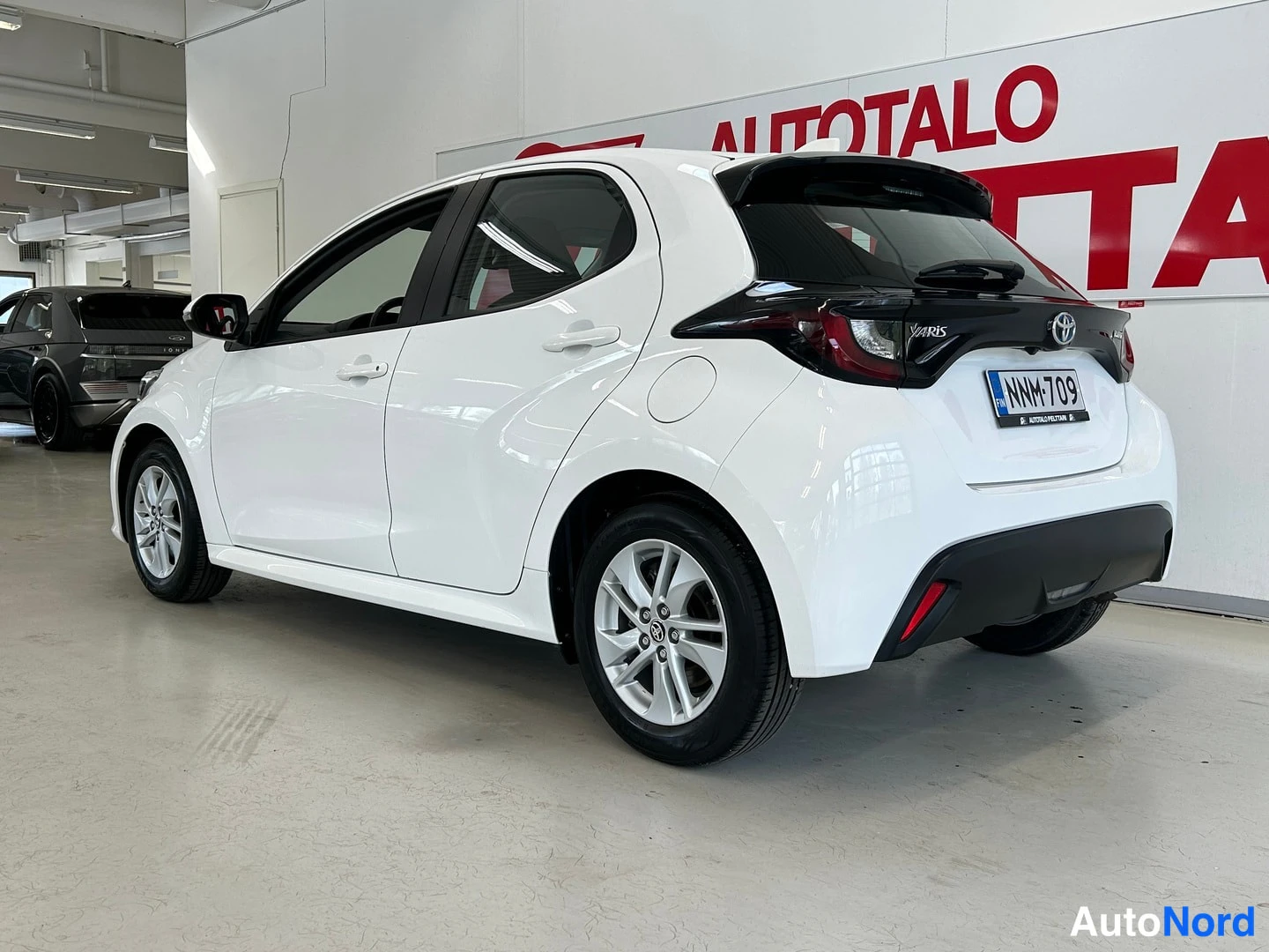 Takaviisto: Valkoinen Toyota Yaris takaa sivulta kuvattuna, rekisteritunnus.