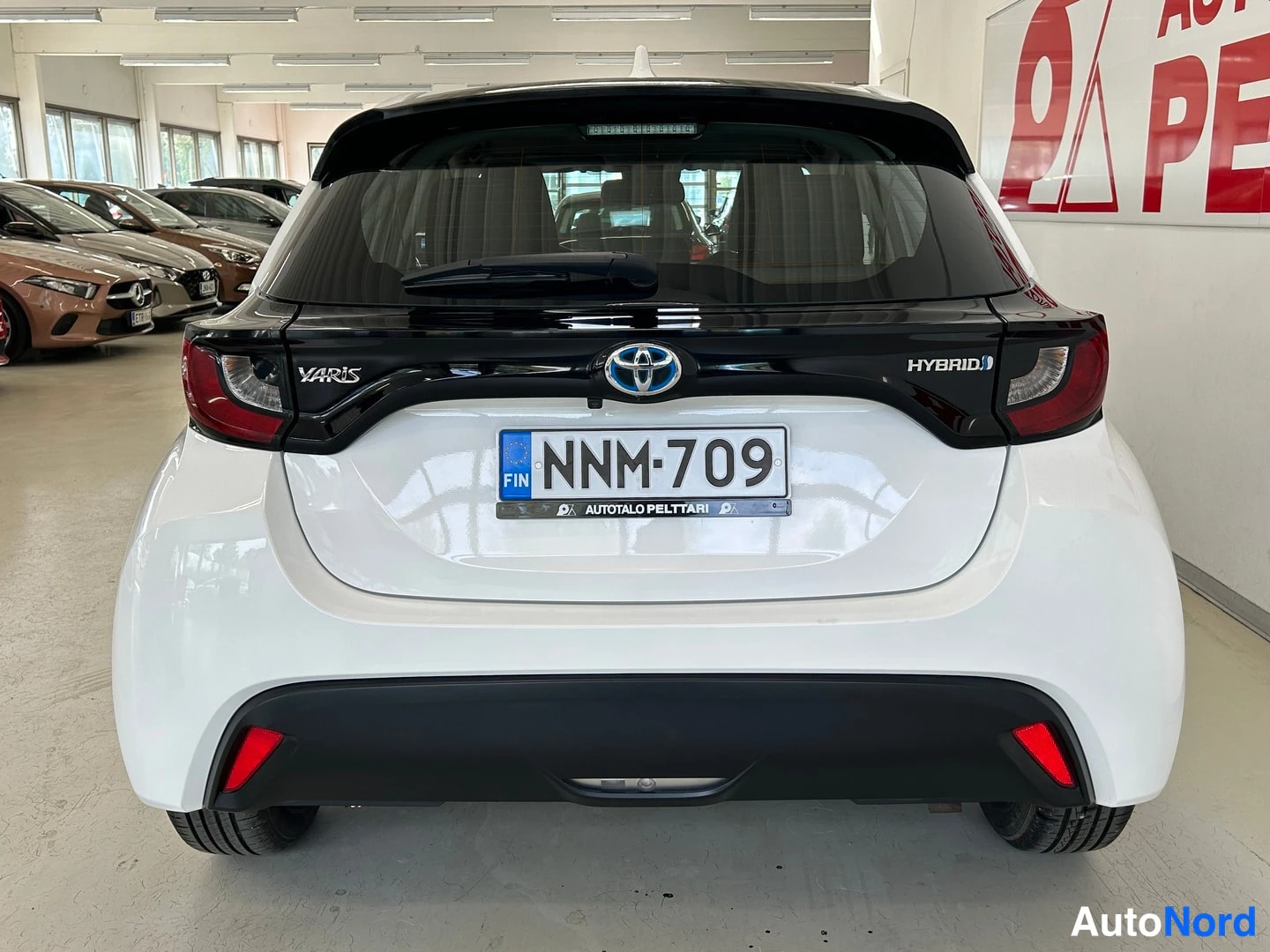 Takaa: Valkoinen Toyota Yaris takaa suoraan kuvattuna, HYBRID-merkintä ja rekisteritunnus.