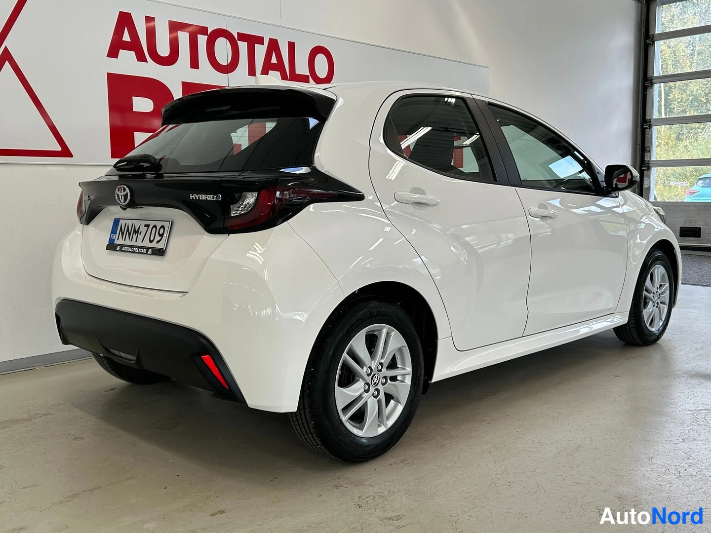 Takaviisto: Valkoinen Toyota Yaris takaa sivulta kuvattuna, rekisteritunnus.