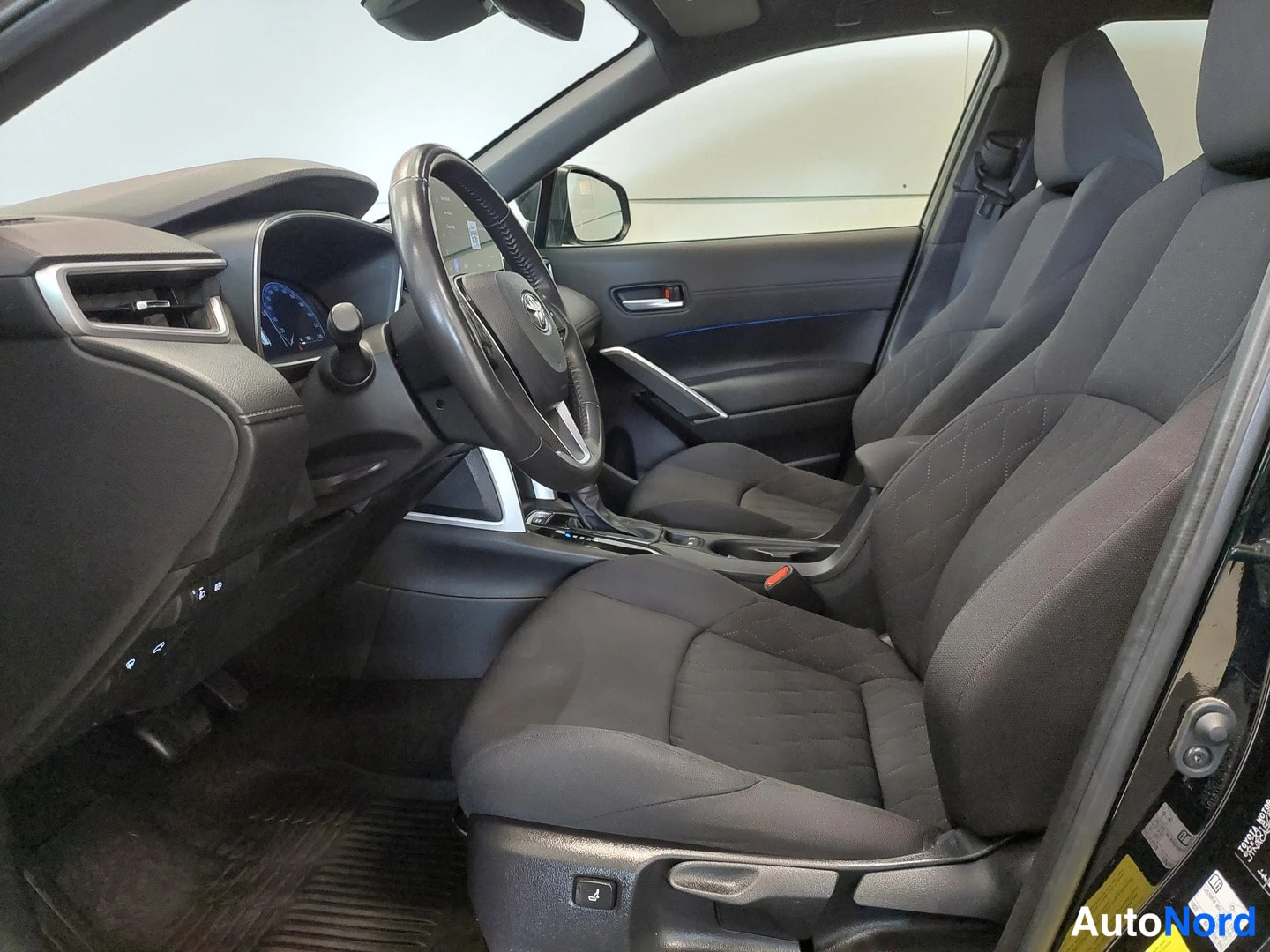 Muu: Auton etupenkkien ja kojelaudan näkymä kuljettajan ovesta; tumma kankaanverhoilu,Toyota-ohjauspyörä ja mittaristo.