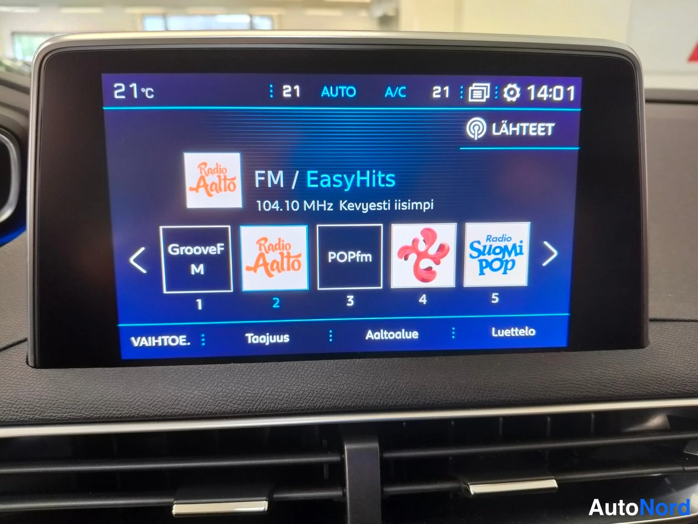 Muu: Infotainment-näyttö näyttää FM-radioasemaa Radio Aalto 104.10 MHz ja ilmastoinnin asetukset 21 astetta A/C.