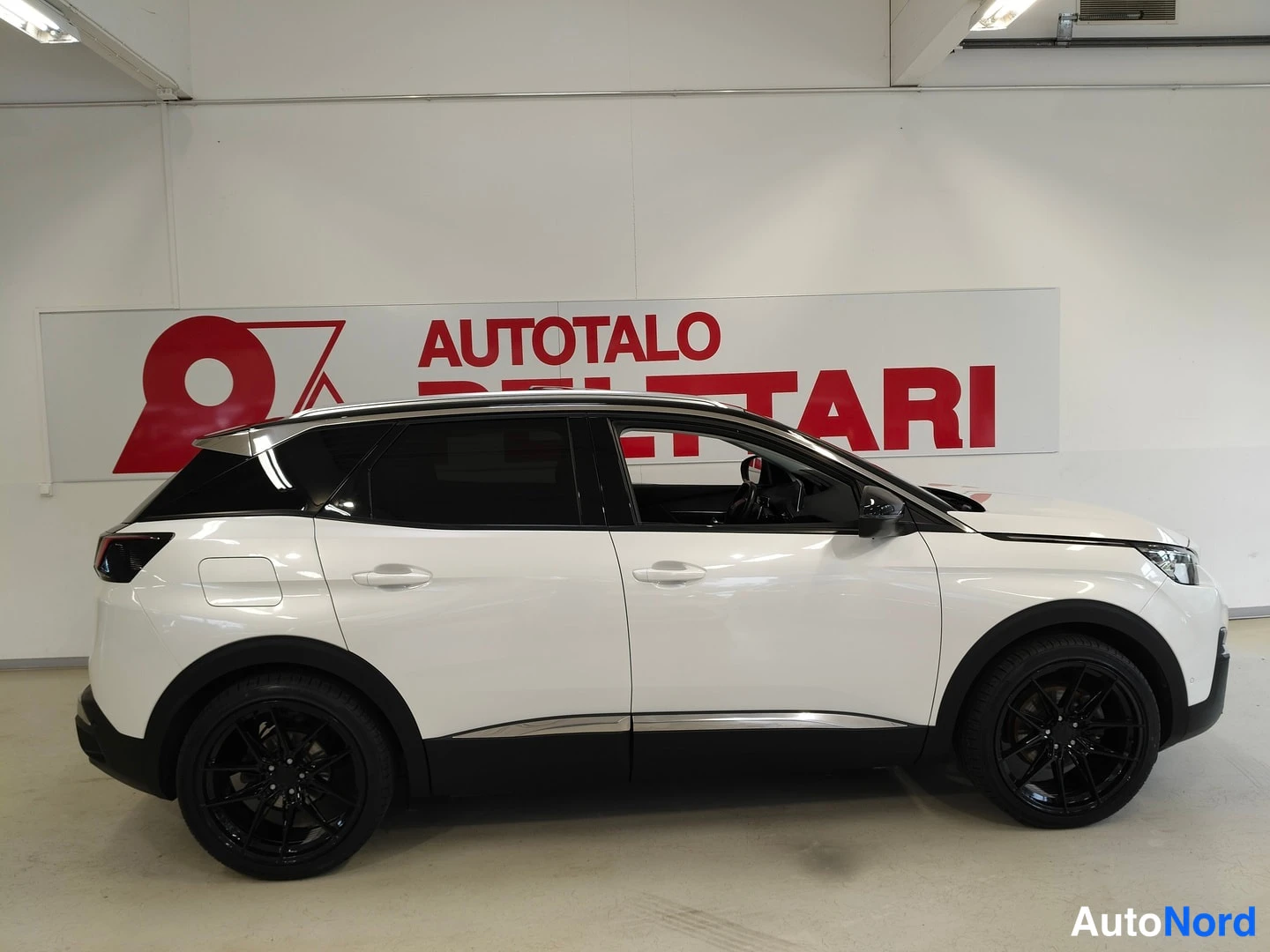 Sivulta: Sivunäkymä valkoisesta Peugeot 3008:sta vasemmalta katsottuna, mustat kattopalkit ja mustat kevytmetallivanteet, taustalla Autotalo Pelttari -kyltti.