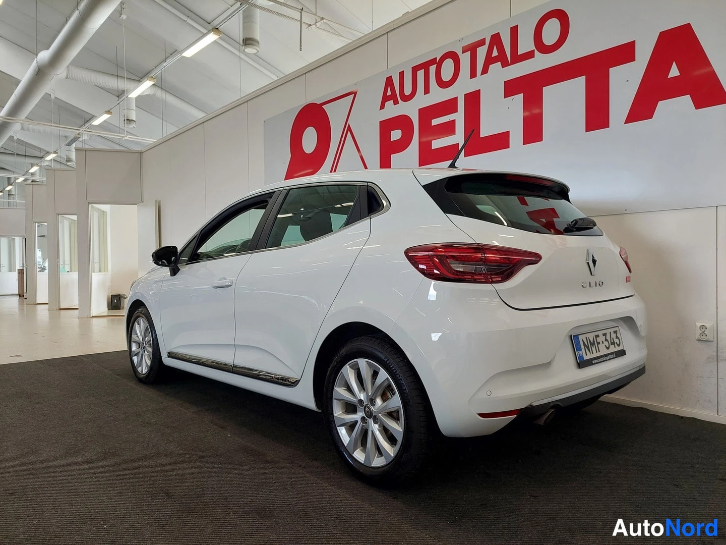 Takaviisto: Valkoinen Renault Clio -henkilöauto takasivukulmasta sisätiloissa, takavalot, CLIO-merkki ja rekisterikilpi näkyvät.