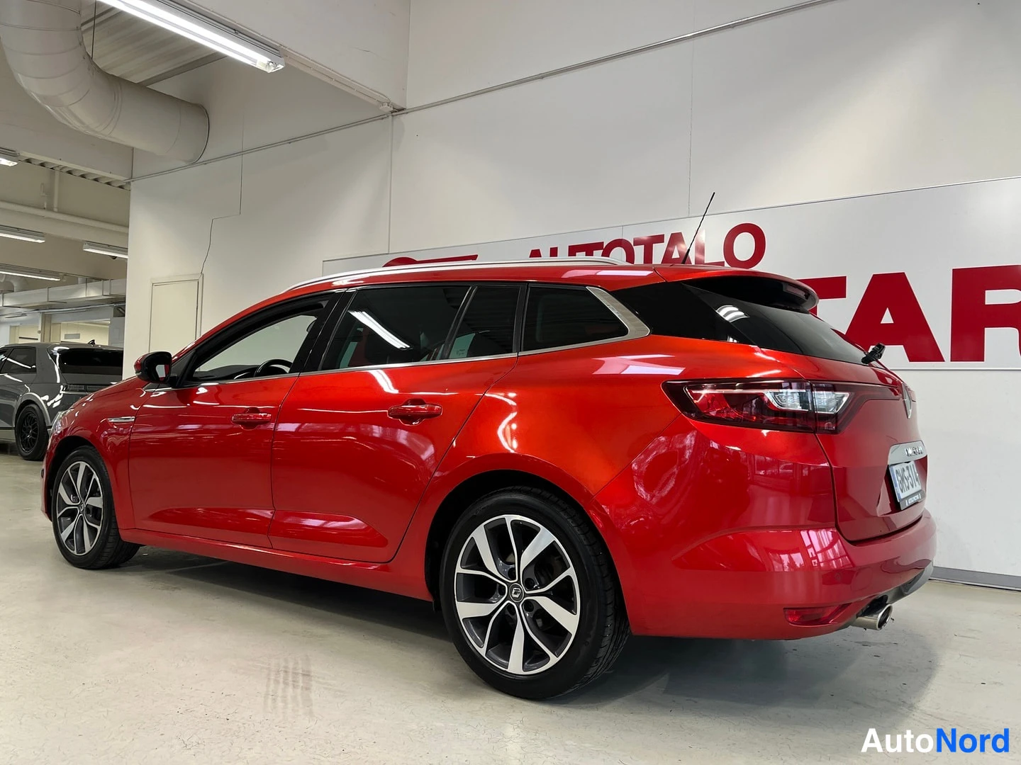Takaviisto: Punaisen Renault Meganen farmarikori takakenakulasta; takavalot, rekisterikilpi ja hopeat vanteet näkyvät.