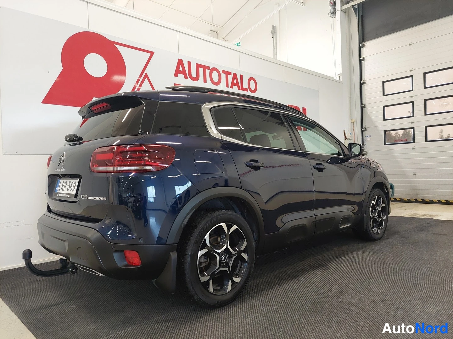 Takaviisto: Tummansininen Citroën C5 Aircross -farmariauto takaa kulmasta sisätiloissa; rekisteri, vetokoulu kiinnitetty.