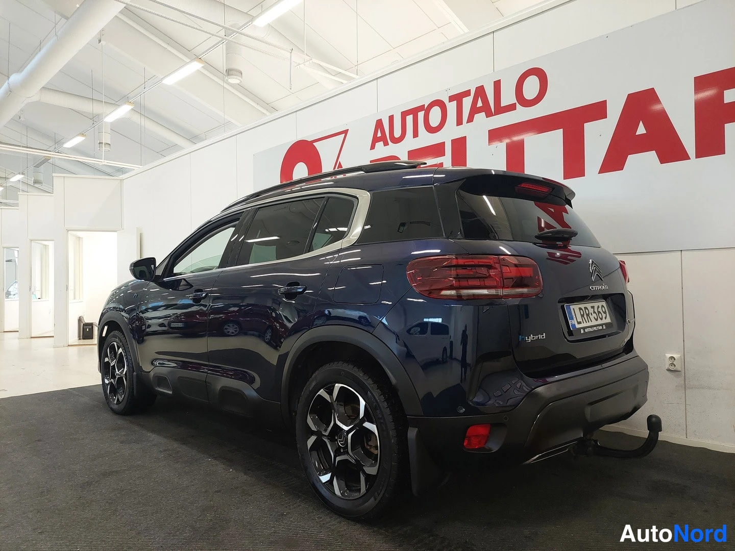 Takaviisto: Tummansinisen Citroën C5 Aircrossin takakulmakuva sisätiloissa, rekisterikilpi RR-369 ja Hybrid-tunnus takaluukussa.