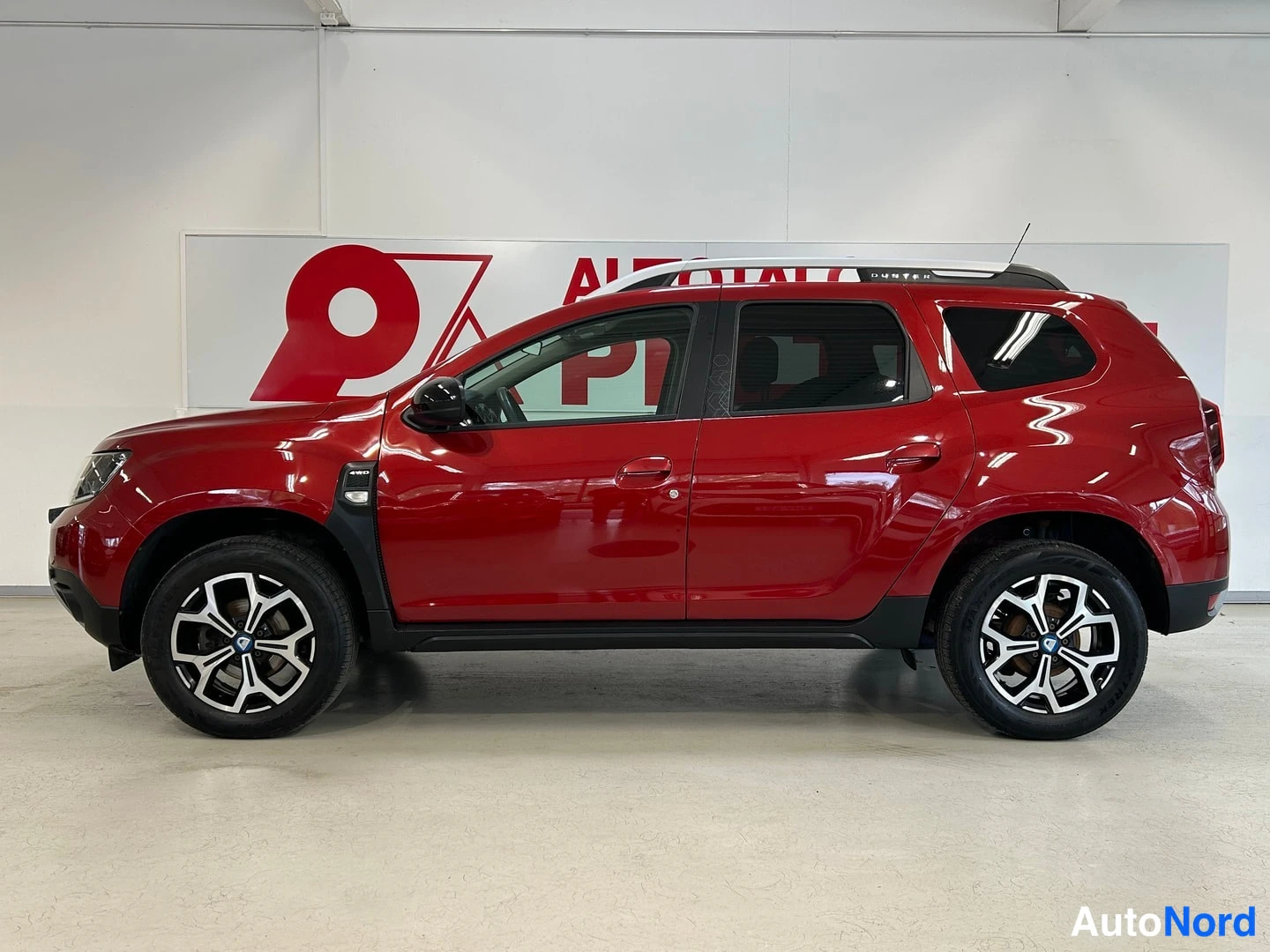 Etuviisto, nokka vasemmalle: Punainen Dacia Duster -henkilöauto sisätiloissa kuvattu kolmivartaloasennossa keulasta vasemmalle.