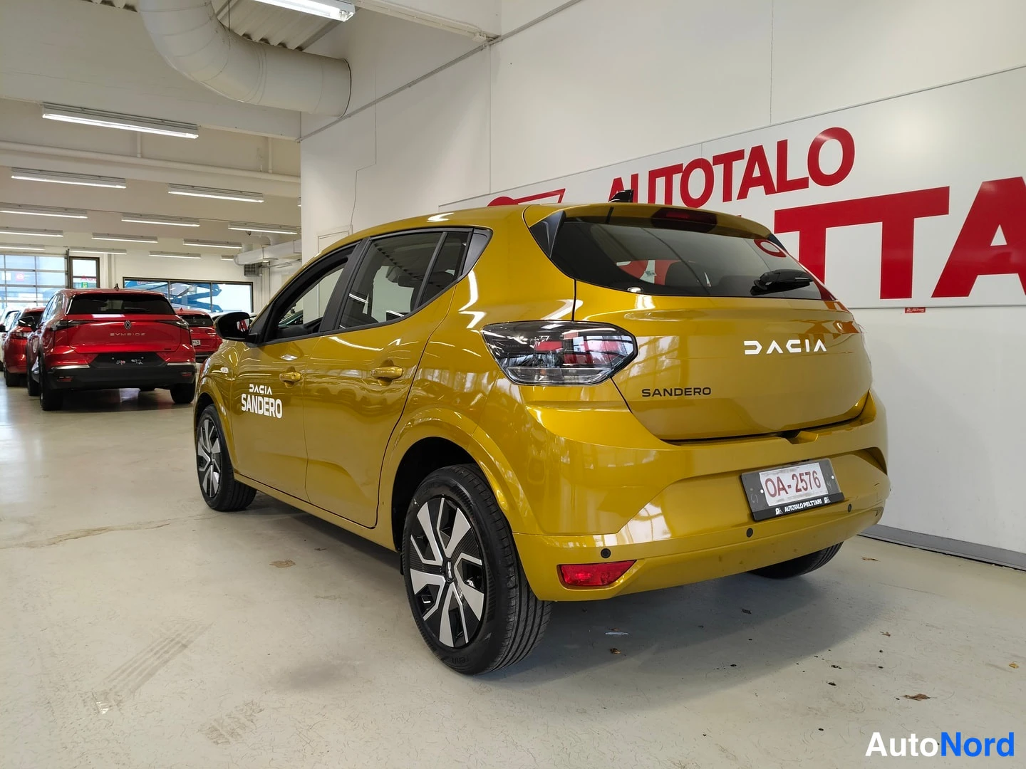 Takaviisto: Dacia Sandero -keltainen hatchback takakulmanäkökulmassa sisätiloissa, rekisterikilpi OA-2576