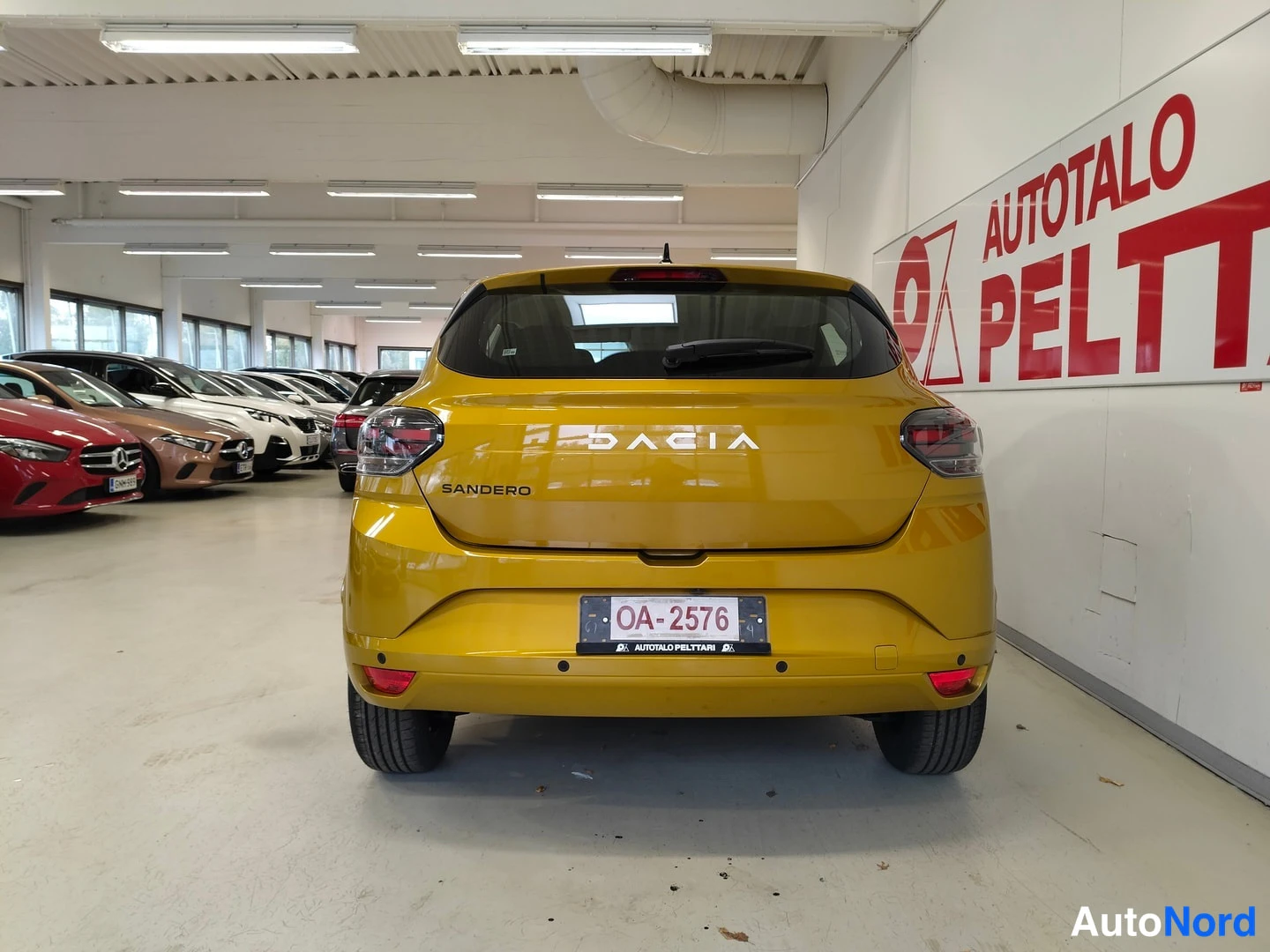 Takaa: Auton takaosa suoraan takaa: keltainen Dacia Sandero, rekisterikilpi OA-2576, DACIA- ja SANDERO-tekstit takaluukussa.