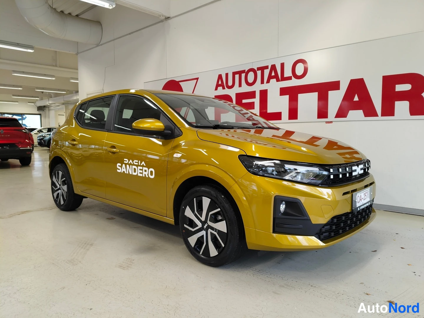 Etuviisto, nokka oikealle: Keltainen Dacia Sandero etuviistosta oikealta: keulalla DACIA-maski, REC-kilpi OA-2576 ja oveen kirjoitettu teksti DACIA SANDERO.