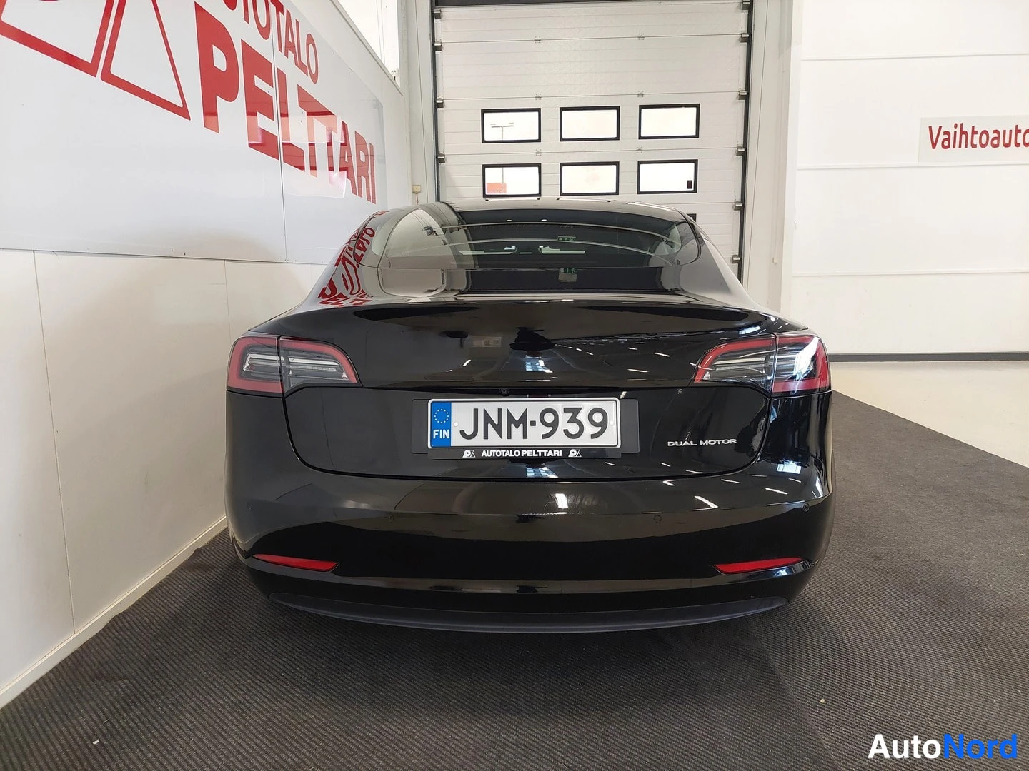 Takaa: Mustan auton takapää suoraan takaa, rekisterikilpi ja DUAL MOTOR -teksti tavaratilan kannessa.