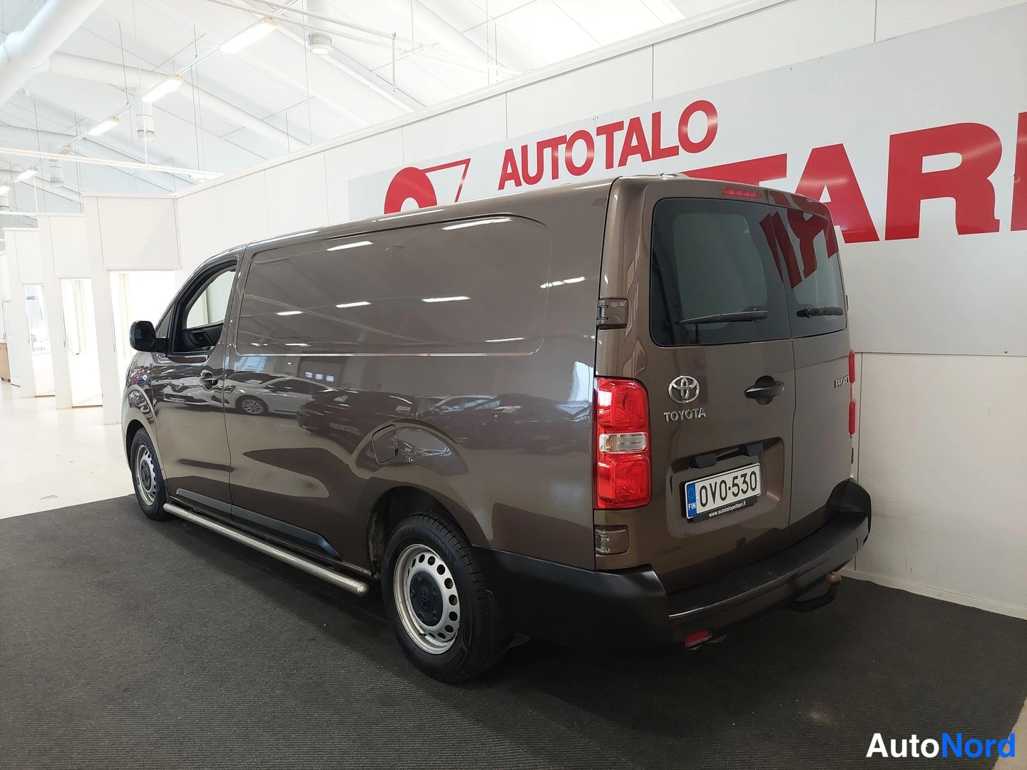 Takaviisto: Taka-kolmasosan kuvakulma Toyota Proace -pakettiautosta, ruskea, rekisteritunnus, kyljessä TOYOTA-merkintä ja takaosan valot näkyvät.