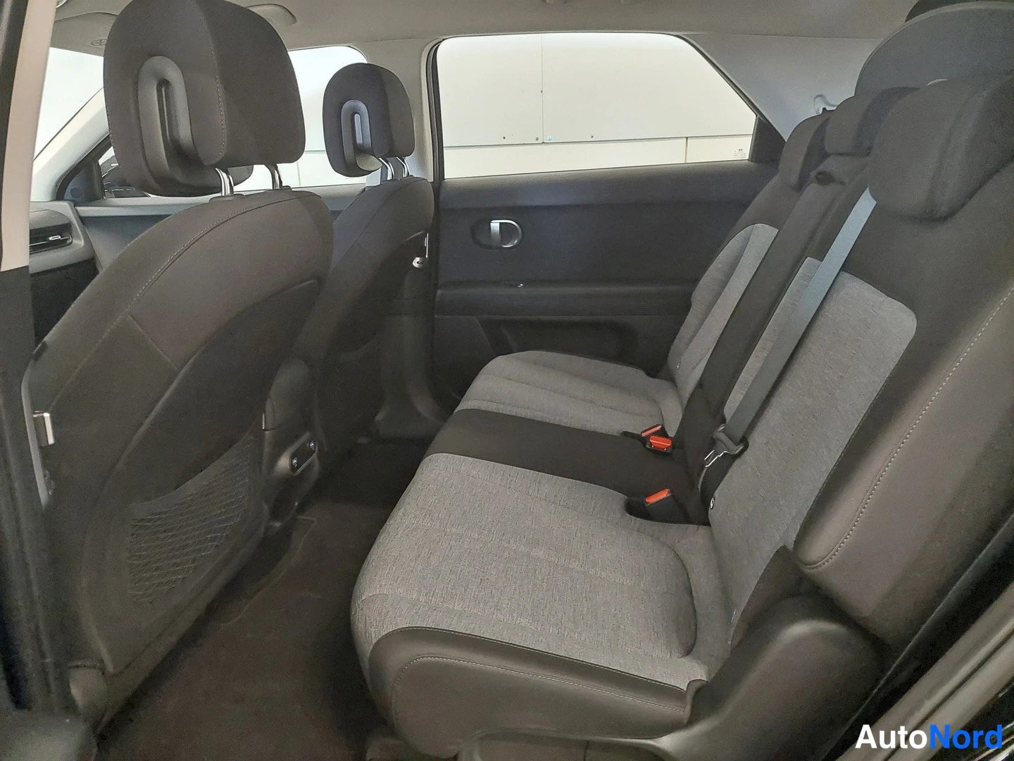 Muu: Hyundai IONIQ 5:n takaistuin ja takamatkustamotila: harmaa kangasverhoillut istuimet, tummat ovi- ja sivupaneelit, avattu takaovi.