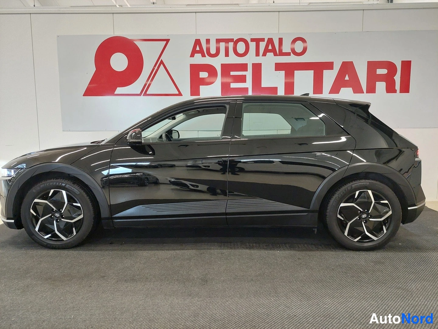 Etuviisto, nokka vasemmalle: Mustan Hyundai IONIQ 5:n kylkinäkymä autosalissa.