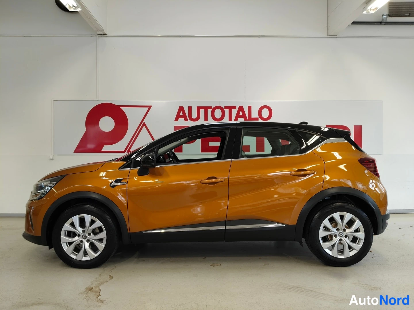 Etuviisto, nokka vasemmalle: Renault Captur -henkilöauto sivulta eteenpäin kuvattuna oranssilla korilla ja mustalla katolla sisätiloissa.