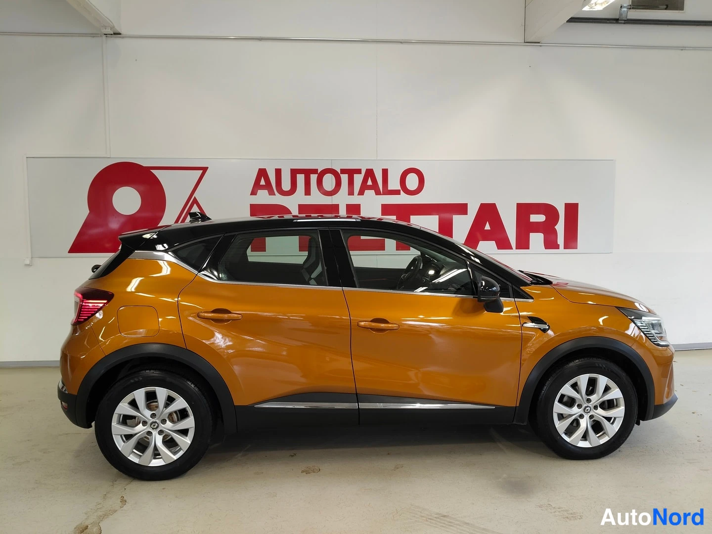 Sivulta: Oranssi Renault Captur sivuprofiilista kuvattuna autonäyttämössä; musta katto ja hopeiset vanteet näkyvät.